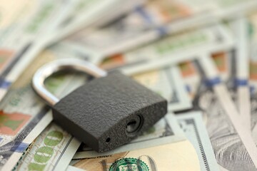 Small black padlock lies on big amount of new hundred US dollar bills