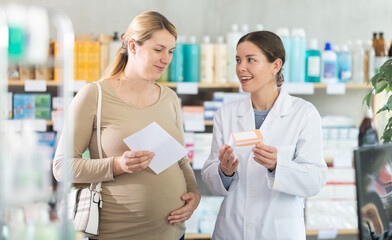 Obraz premium Young female pharmacist giving prescription pills to pregnant woman in pharmacy