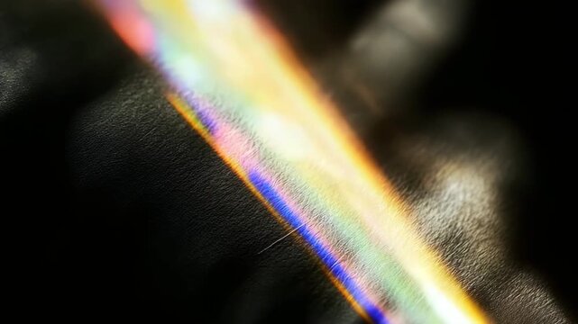 Animation of light refraction with rainbow spectrum on dark background. Colorful abstract texture resembling optical diffraction across metal surface.