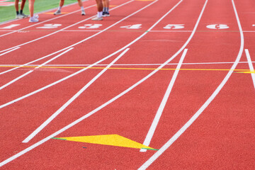 unrecognizable athletes gather on a red running track, preparing at the starting lanes for training or competition.