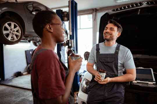 Two mechanics enjoying a break while discussing car repairs in an auto shop