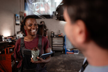 Technician smiles while assisting customer in auto repair shop during daytime