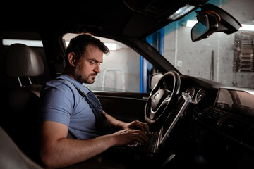 Obraz premium Mechanic working on a laptop inside a vehicle at an auto shop during the day