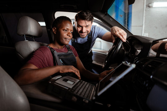 Two mechanics working together on a car's diagnostic system in an auto shop - Powered by Adobe