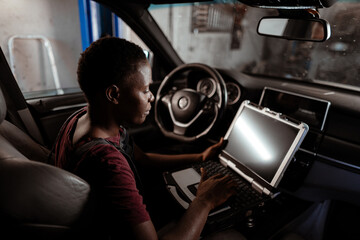 Young mechanic working on a laptop inside a vehicle in an auto shop during the day