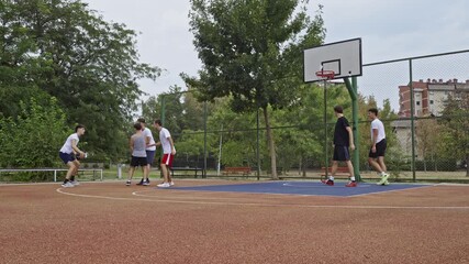Male teenagers enjoying a friendly game of basketball on an outdoor court in their neighborhood. These friends are actively playing and showcasing their skills, emphasizing teamwork and casual fun. - Powered by Adobe