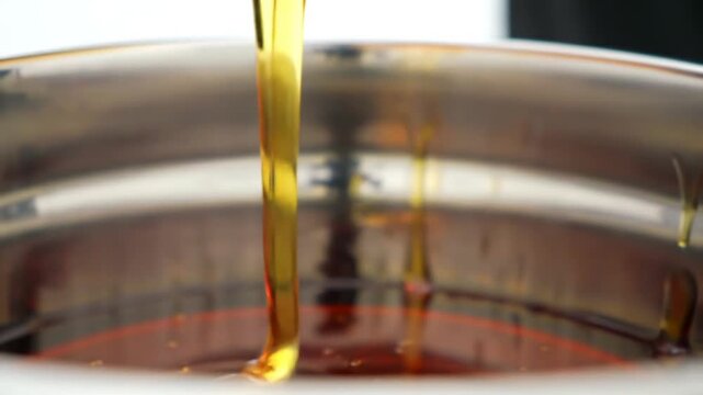 Close Up of Golden Corn Syrup Pouring Thickly into Stainless Steel Bowl in Soft Lighting Creates a Visually Appetizing Scene Suitable for Food Advertisements and Culinary Demonstrations Featuring