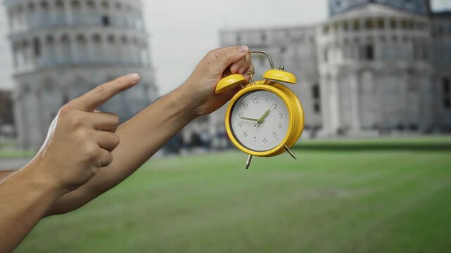 Man holding yellow clock pointing against pisa tower showcasing time concept in italy city outdoor setting.