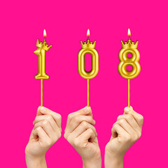 Birthday on a fuchsia background with the number 108 - Hands holding number-shaped candles