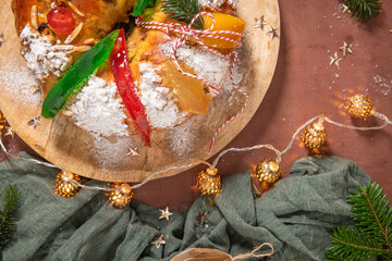Colorful candied fruits and powdered sugar on a traditional Bolo Rei or Kings Cake, set on a wooden board amidst warm holiday decorations and lights. Is tradicional for Christmas in Portugal. Top view