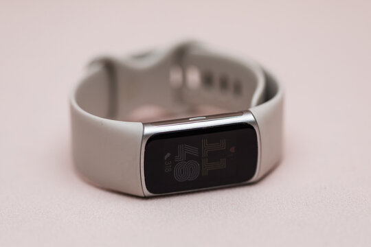 Closeup of a fitbit smartwatch charge 6 with a beige band on blush pink background