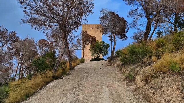 A scenic view of an ancient stone tower along a winding path, framed by vibrant trees and a clear blue sky