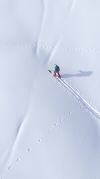 TOP DOWN: Flying above a split boarder trekking uphill on a sunny winter day. Young female tourist snowshoes up a snowy hill during an off piste snowboarding trip in the idyllic Slovenian mountains.