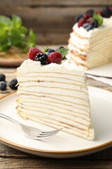 Piece of tasty crepe cake with berries served on wooden table, closeup