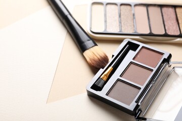 Colorful eyeshadow palettes and makeup brush on beige background, closeup. Space for text