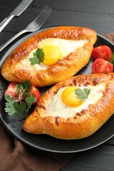 Tasty khachapuri with cheese and eggs served on black wooden table, closeup