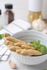 Pickled asparagus spears with spices in bowl on white table, closeup