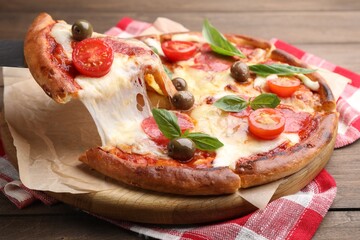 Taking piece of delicious pizza with cheese, salami, tomatoes and olives at wooden table, closeup