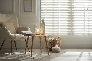 Stylish lamp, vase and books on wooden table near armchair indoors, space for text