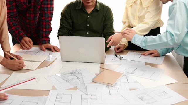Architect and safety engineer discussion about building blueprint displaying on laptop on table with architectural document and wooden block scatter around at modern office. Closeup. Delineation.