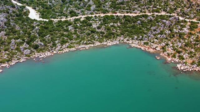 aerial drone shot captures the historic Simena Castle Kalek&ouml;y on Turkey's Mediterranean coast, overlooking the crystal-clear turquoise waters of Kekova. The footage showcases the ancient ruins nestled