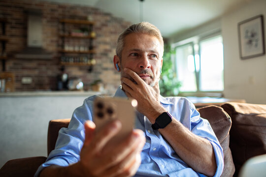 Thoughtful man using smartphone at home