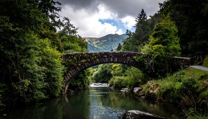 An old stone bridge arches over a flowing river, surrounded by lush green vegetation and distant mountains under a cloudy sky
