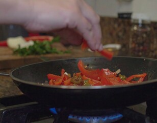 Person adding sliced red peppers to a pan of cooking vegetables