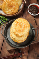 Golden Flaky Layered Bun Bread in Cast Iron Pan with Dipping Sauce on Wooden Table