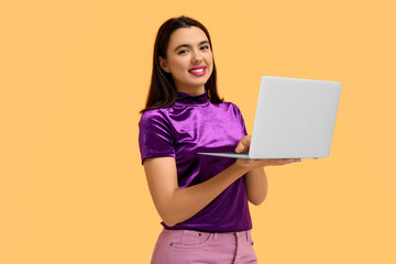Naklejka premium Beautiful young happy woman with laptop on yellow background