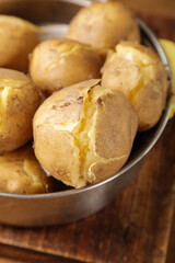 Fresh Cooked Potatoes with Cracked Skins in Metal Bowl Closeup on Wood Surface