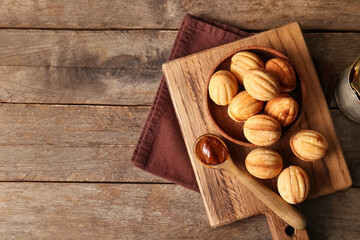 Cutting board with tasty walnut shaped cookies and boiled condensed milk on wooden background