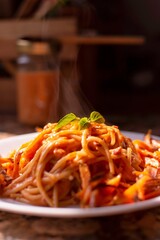 Plate of spaghetti with rich tomato sauce, garnished with a fresh basil leaf. Sunlight shines on...
