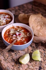 Bowl of traditional Mexican pozole on a rustic kitchen table. Authentic homestyle dish with corn, broth and toppings. Warm, cultural and comforting Mexican food photography.