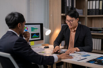 Two men are sitting at a desk with a computer monitor in front of them