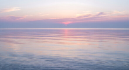 Fototapeta premium Calm ocean water reflects the soft colors of a pastel sunset, with the sun partially obscured by clouds on the horizon.