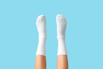 Legs of young woman in white cotton socks on blue background