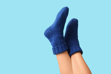 Legs of young woman in blue knitted socks on color background