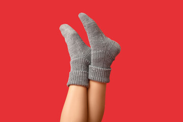 Legs of young woman in grey knitted socks on red background