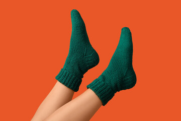 Legs of young woman in green knitted socks on orange background