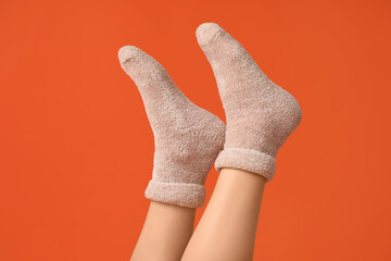 Legs of young woman in warm beige socks on orange background