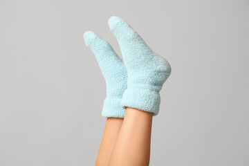 Legs of young woman in warm blue socks on grey background