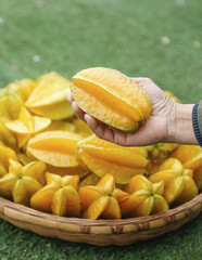Fresh Star Fruit Carambola in Hand with Basket of Ripe Yellow Tropical Fruit Slices on Grass