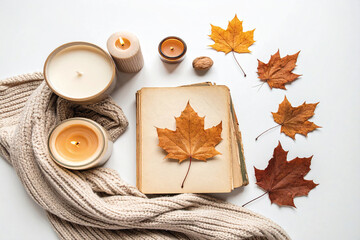 Cozy autumn flat lay with candles, dried maple leaves, and a knitted scarf creating a warm seasonal atmosphere.
