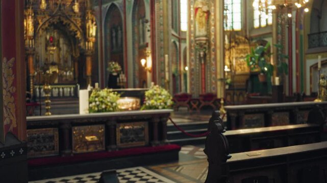 Defocused image of an ornate catholic church interior featuring intricate architecture and colorful stained glass windows highlighting religious decor and floral arrangements.