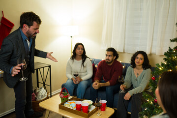 Sad and drunk man looking upset and having a discussion in a christmas party with friends