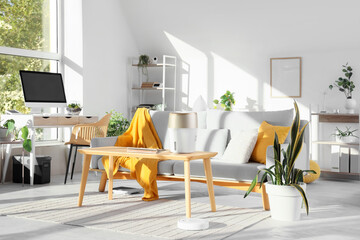 Interior of light living room with sofa, workplace and appliances