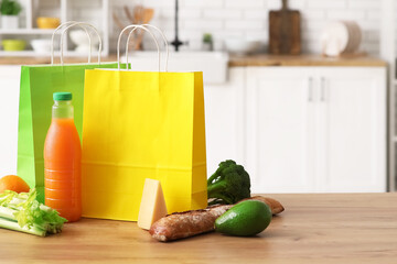Paper bags with different fresh products on wooden table in kitchen