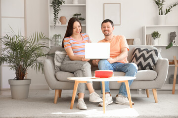 Obraz premium Happy couple relaxing on sofa with laptop, enjoying online content together in bright living room