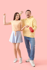 Young couple with portable speaker dancing on pink background